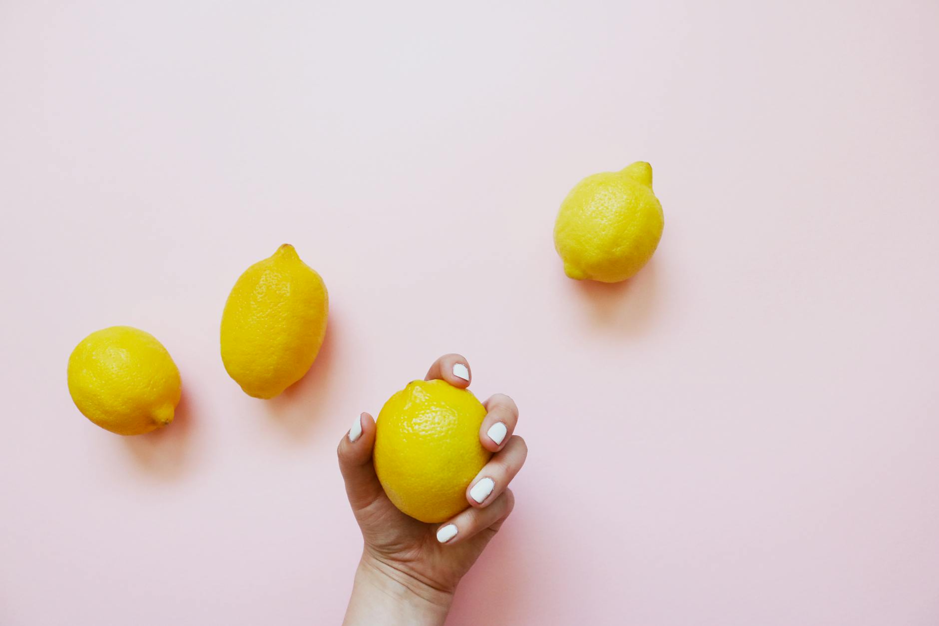 Hand holding a fresh lemon on soft pink background with additional lemons, symbolizing natural pleasure and arousal